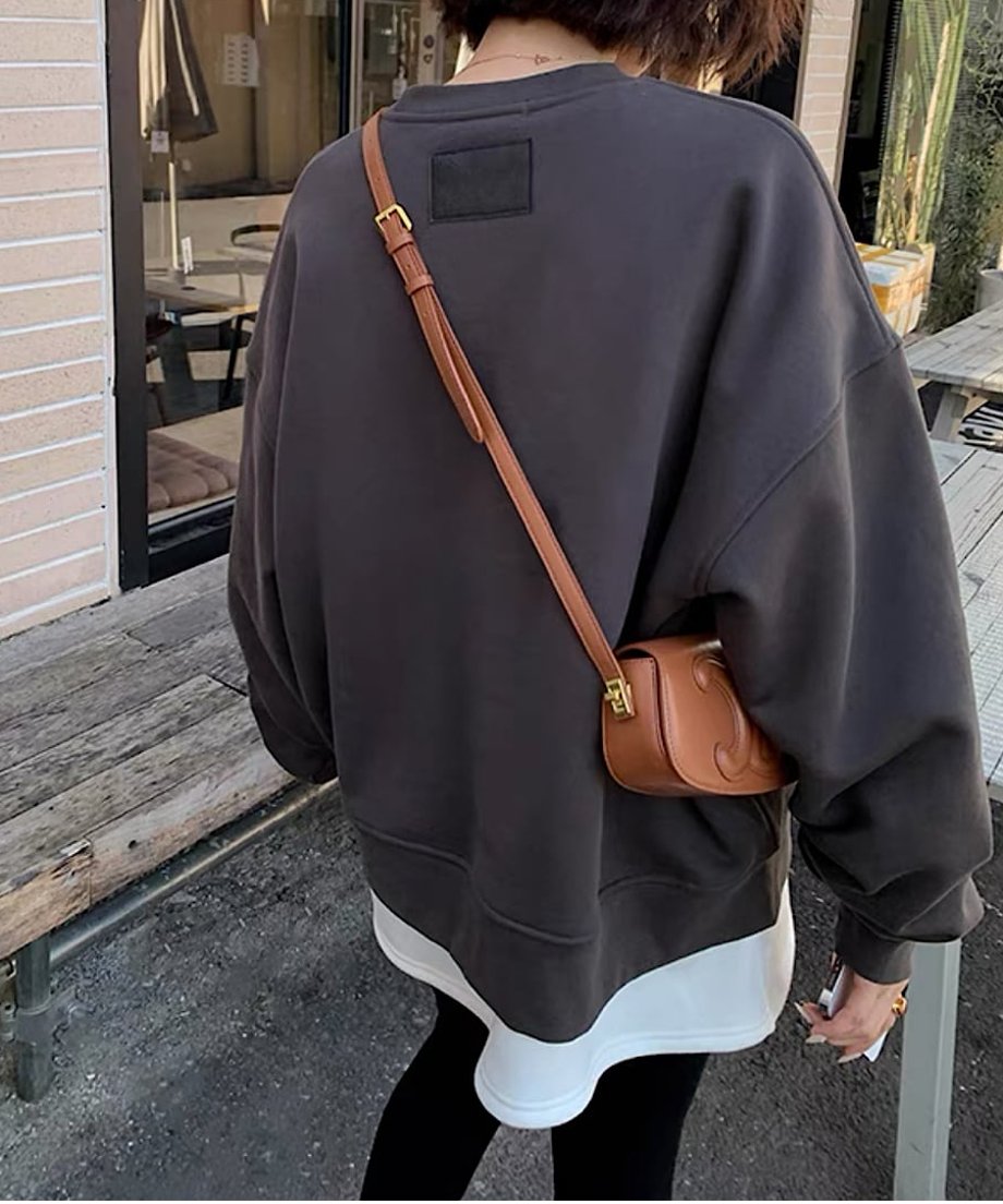 グレーのオーバーサイズスウェットを着用した後ろ姿。首元下に黒いレザー調のスクエアタグが付いています。