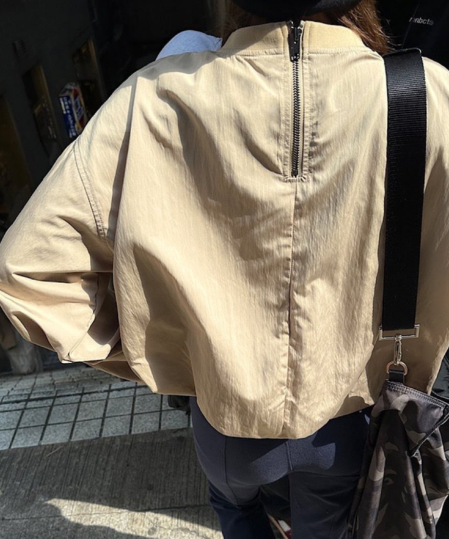 ベージュのバックジッププルオーバーを着た女性の後ろ姿。