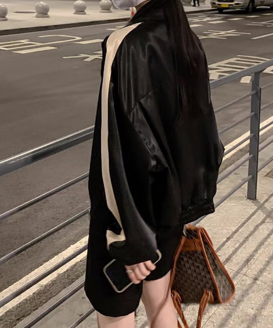 黒のバイカラーブルゾンを着た女性の背中側からの全身像。肩から背中にかけて入るベージュの太いラインが目立ち、黒のボトムスを着用し、茶色の柄入りバッグを持っている。