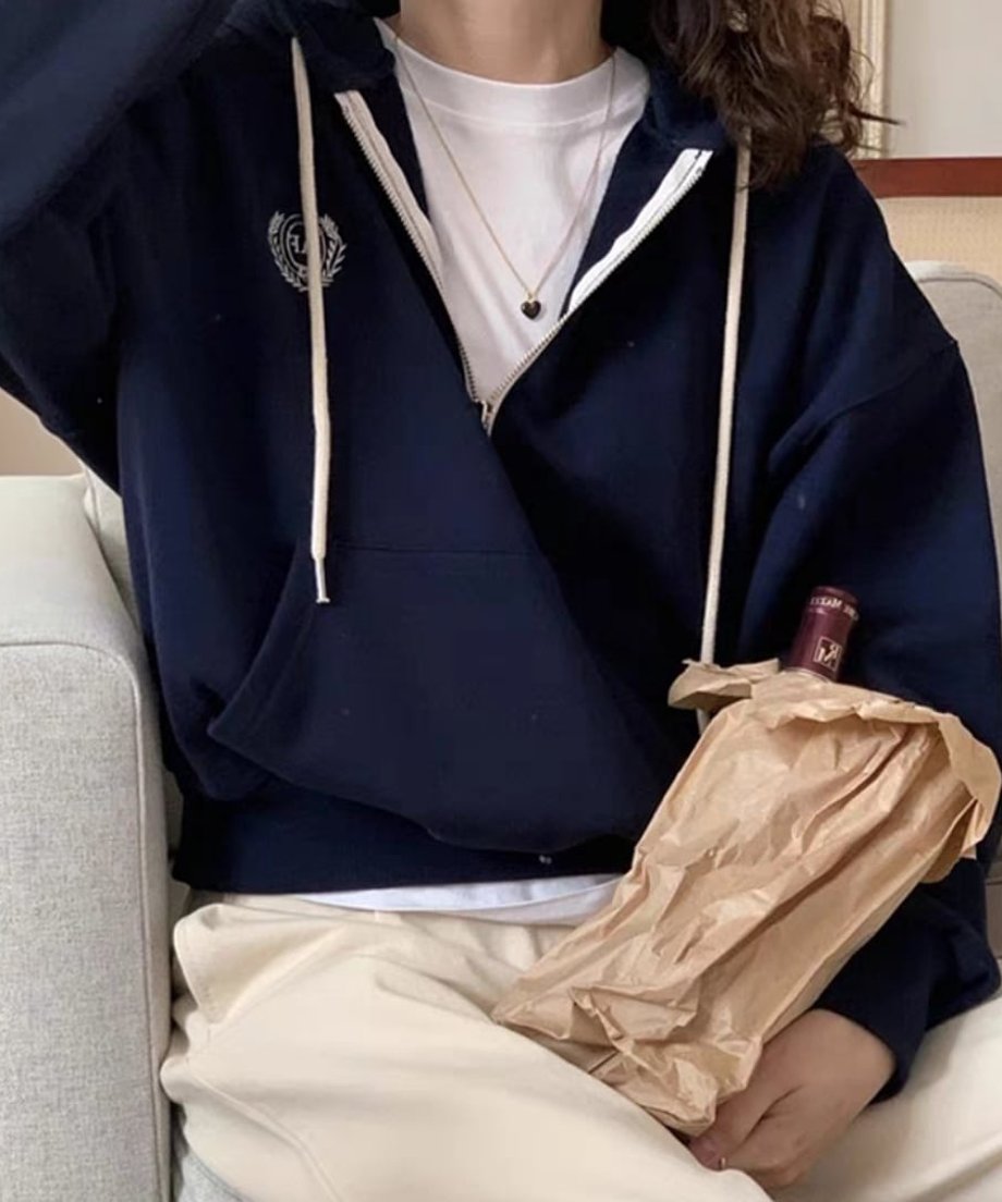 ネイビーのハーフジップパーカーを着用した女性が椅子に座っている。インナーは白Tシャツ、ボトムスは生成り色のワイドパンツをはいている。