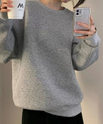 グレーのオーバーサイズスウェットを着用した女性の全身。黒のボトムスを着用し、シンプルなカジュアルスタイルです。手にはカップとスマホを持っている。
