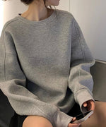 グレーのオーバーサイズスウェットを着用し、黒のショートパンツを合わせた女性。片手にスマートフォンを持っている。
