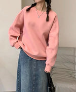 ピンクのオーバーサイズスウェットを着用し、デニムのボトムスと黒のキルティングバッグを合わせた女性の上半身。三つ編みにネックレスを着用しています。