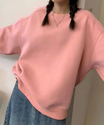 ピンクのオーバーサイズスウェットとデニムのボトムスを着用した女性のアップ。両手を広げてポーズをとっています。