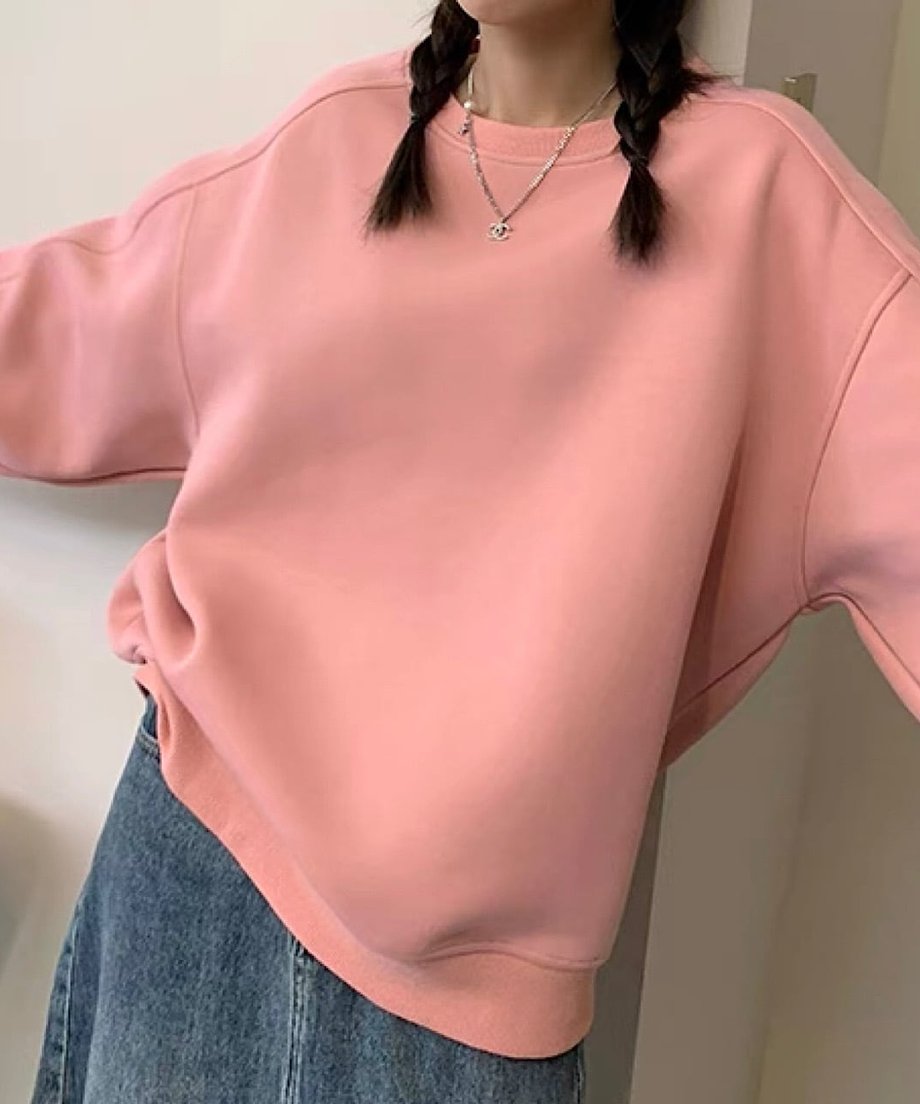 ピンクのオーバーサイズスウェットとデニムのボトムスを着用した女性のアップ。両手を広げてポーズをとっています。
