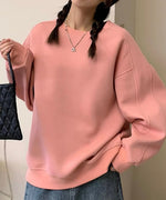 ピンクのオーバーサイズスウェットとデニムのロングスカートを着用した女性の全身。室内で撮影されており、カジュアルでフェミニンなコーディネートです。