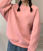ピンクのオーバーサイズスウェットとデニムのロングスカートを着用した女性の全身。室内で撮影されており、カジュアルでフェミニンなコーディネートです。