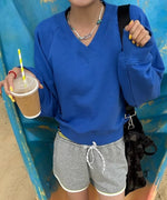 ブルーのVネックプルオーバーとグレーのショートパンツを着用した女性がドリンクを片手に持ったショット。