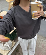 Vネックのチャコールグレースウェットシャツを着た女性が屋外でコーヒーカップを持っている写真。