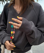グレーのVネックスウェットを着た女性が、カラフルなビーズのブレスレットを持っている手元のクロースアップ。