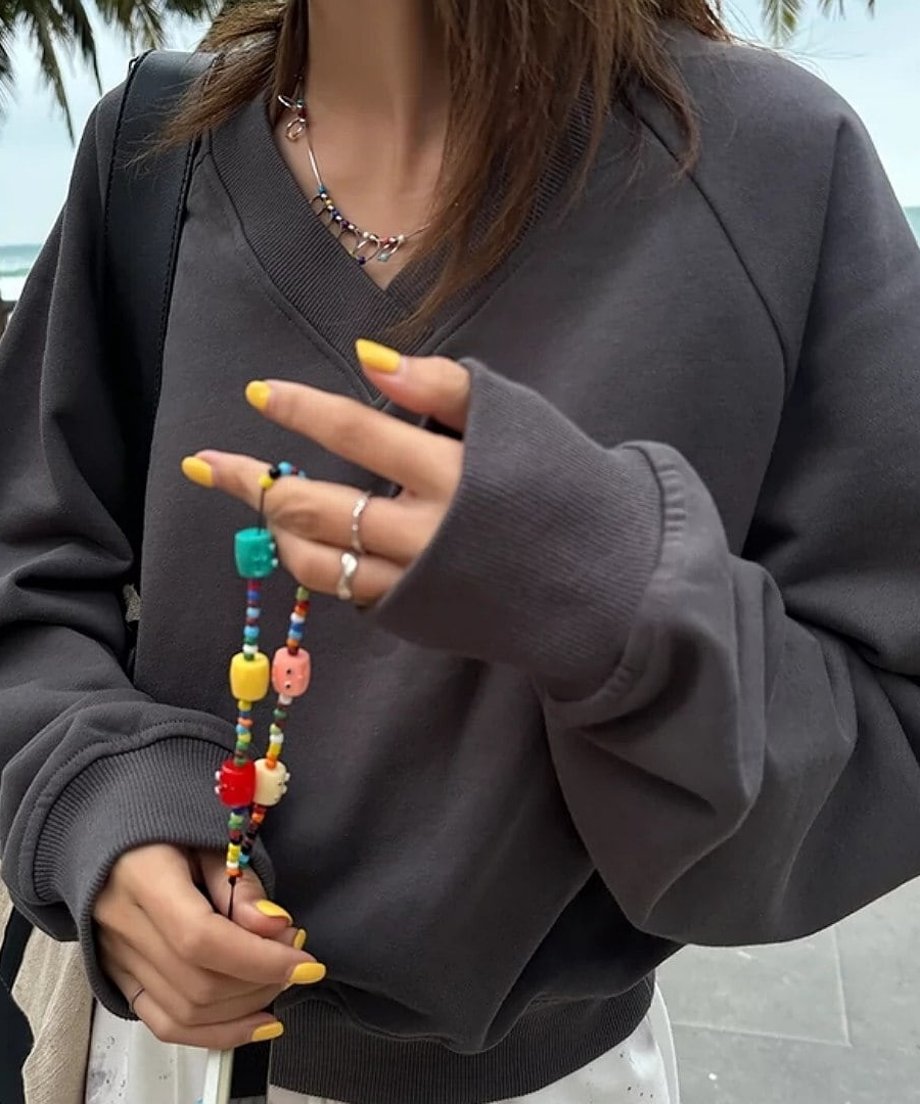 グレーのVネックスウェットを着た女性が、カラフルなビーズのブレスレットを持っている手元のクロースアップ。