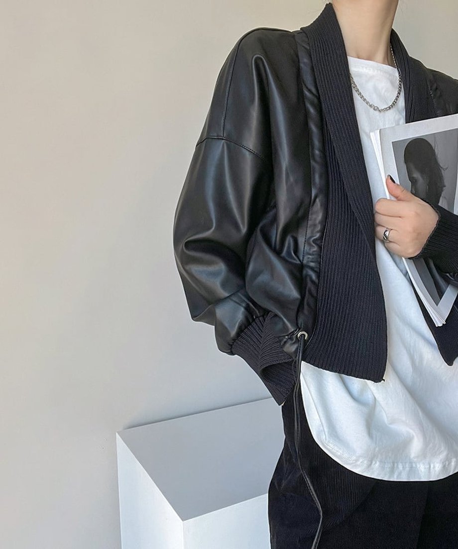 黒のレザージャケットを着用した女性が雑誌を抱えたショット。ショールカラーとリブニットの部分のディティールがわかる。