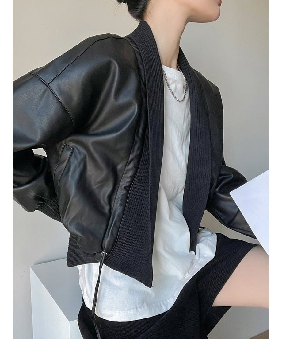 黒いジャケットを着用し、白いタートルネックのインナーとデニムを合わせた女性の斜めからのショット。