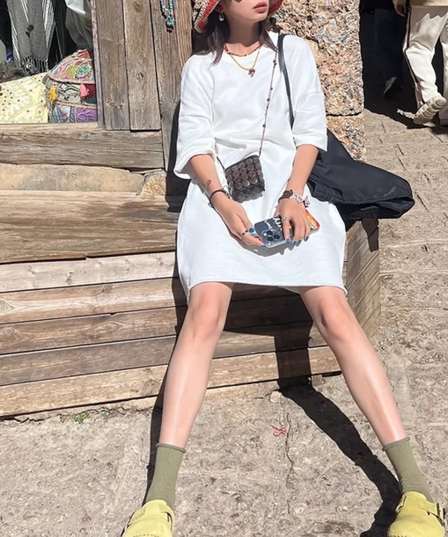 ホワイトのワンピースを着て、木製のベンチに座っている女性。足元は靴下とサンダル。
