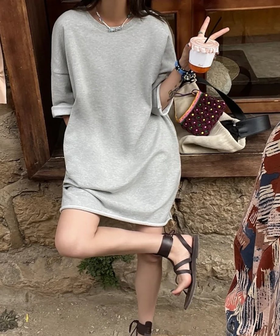 グレーのワンピースを着用し、袖をロールアップしている女性。笑顔で店先のような場所に立っている。