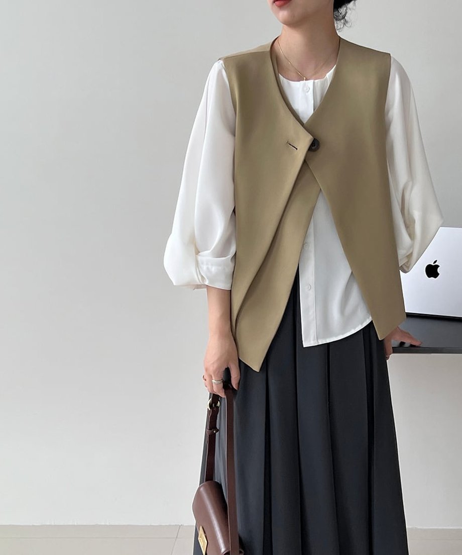 黒のワンボタンクロスベストを着用した女性の全身。ベージュのプリーツスカートとのコントラストが際立つ。