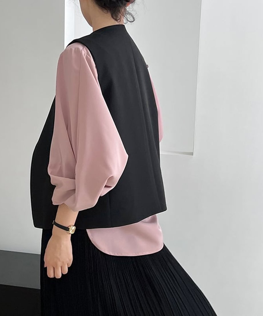 黒のワンボタンクロスベストを着用した女性の後ろ姿。スモーキーピンクのブラウスを合わせている。