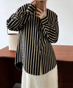 ブラックにベージュのストライプの入ったシャツを着た女性がスマホを持って立っている室内ショット。