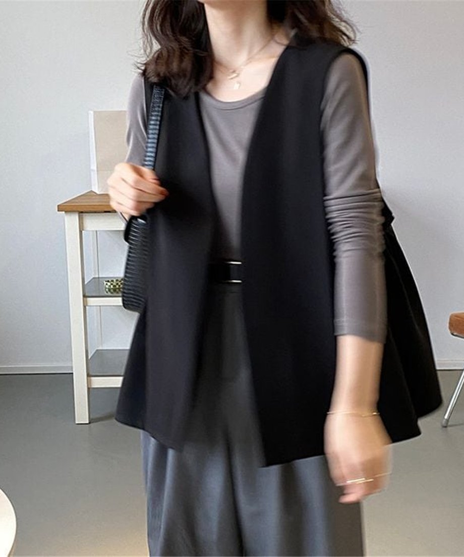 黒のロングベストを着用した女性の正面。グレーの長袖Tシャツとグレーのスラックスに黒のベルトを合わせた女性の室内ショット。
