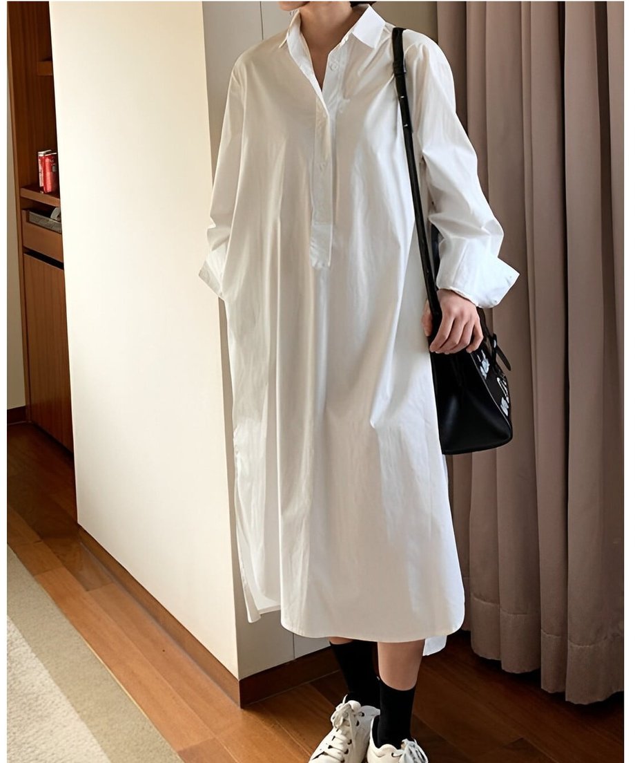 白いテールカットのシャツワンピースを着て、黒いショルダーバッグを提げた女性の全身カット。