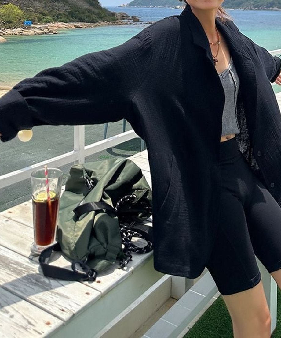 海辺のデッキで、黒のルーズな質感のジャケットを羽織り、リラックスしたひとときを過ごす様子。