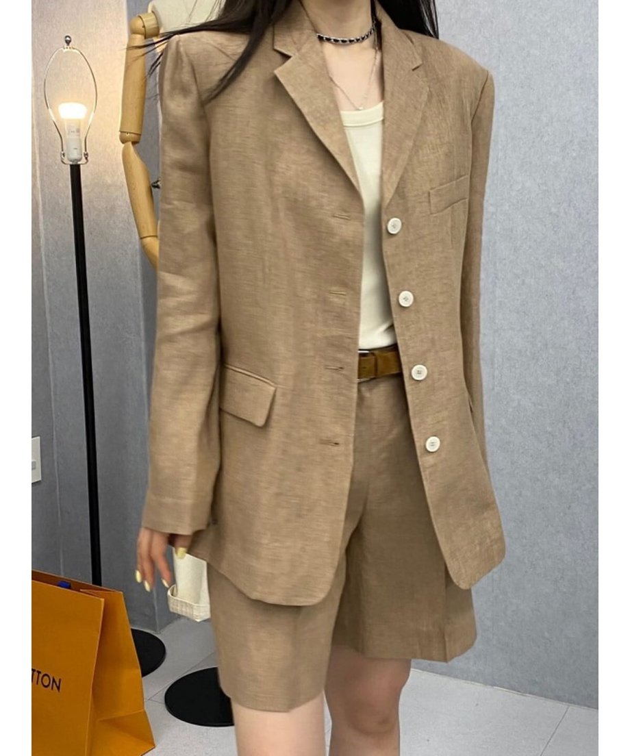 カーキのリネン混セットアップを着用した女性。白いタンクトップとブラウンのレザーベルトを合わせた、大人っぽいきれいめカジュアルなスタイル。