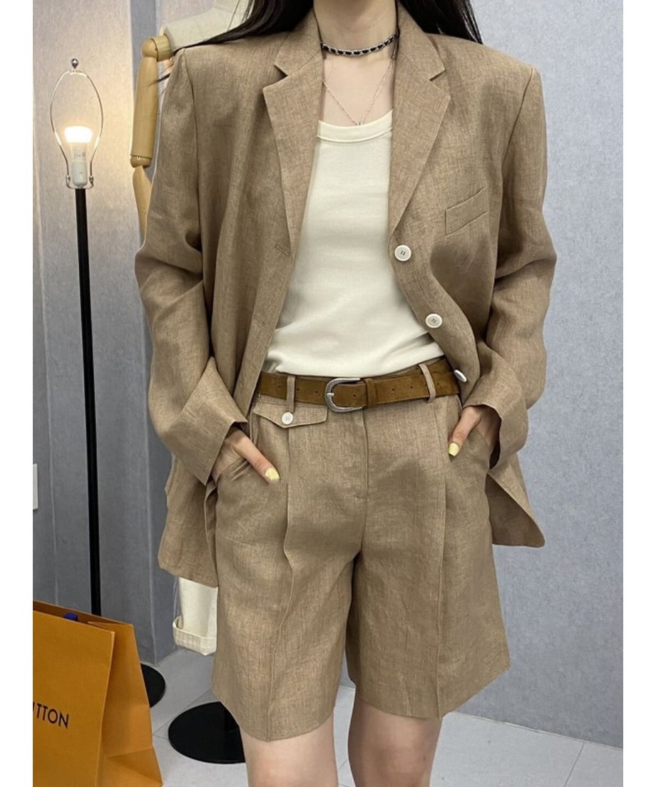 カーキのリネン混セットアップを着用した女性。白いタンクトップとブラウンのレザーベルトを合わせポケットに手を入れたスタイル