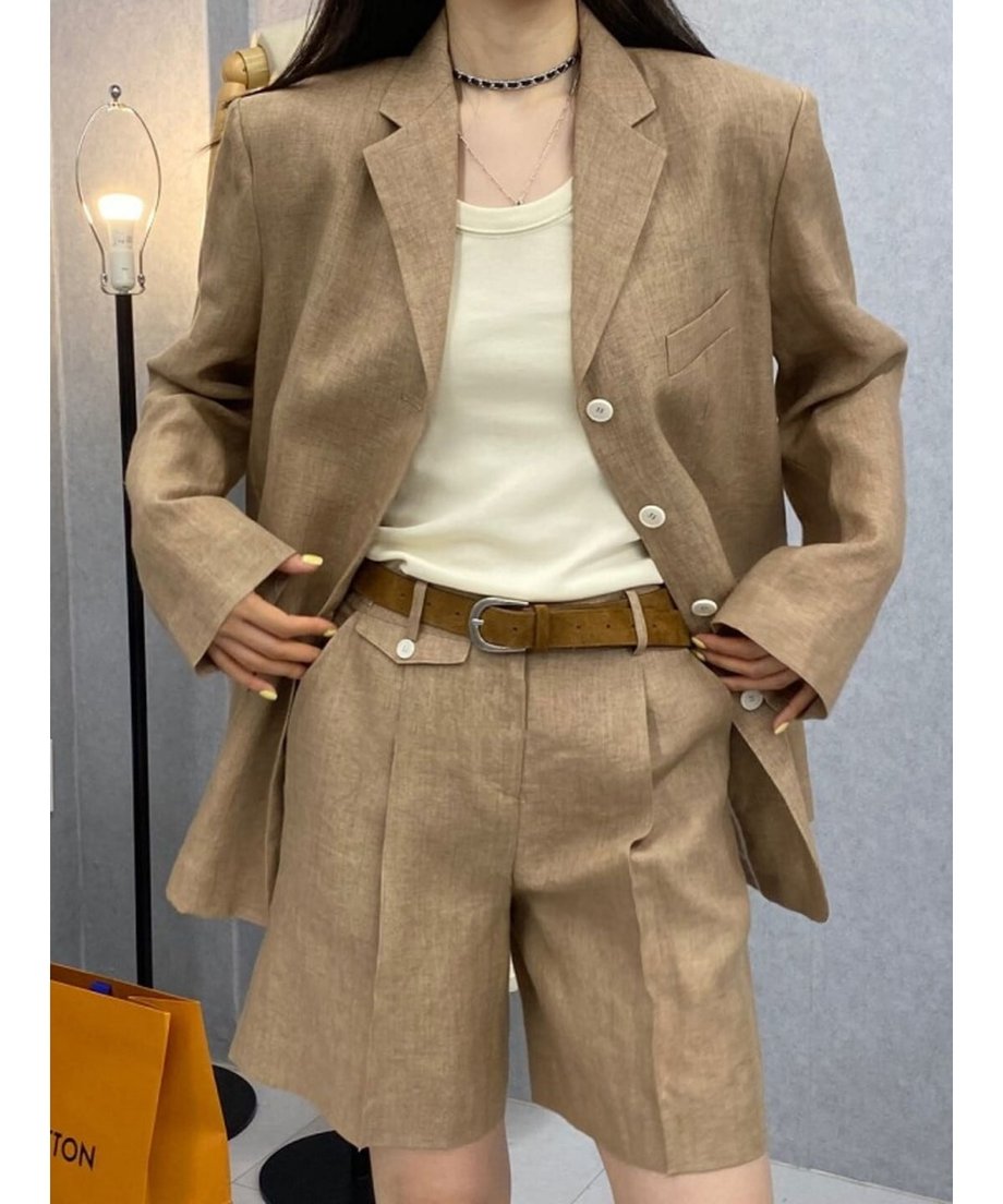 カーキのリネン混セットアップを着用した女性。白いタンクトップとブラウンのレザーベルトを合わせたスタイル。