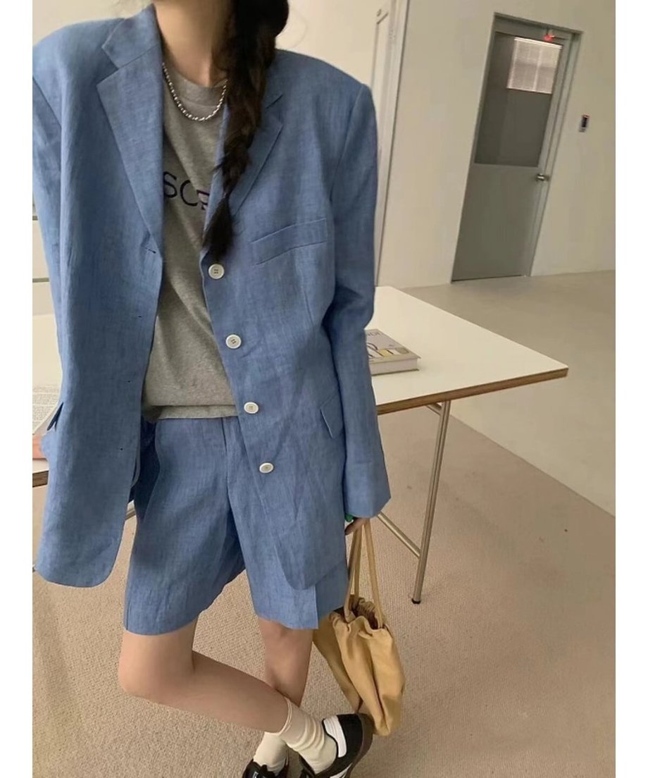 ブルーのセットアップを着用した女性のショット。タック入りのバミューダパンツとジャケットのボタンが４つ並んだデザインがわかる。