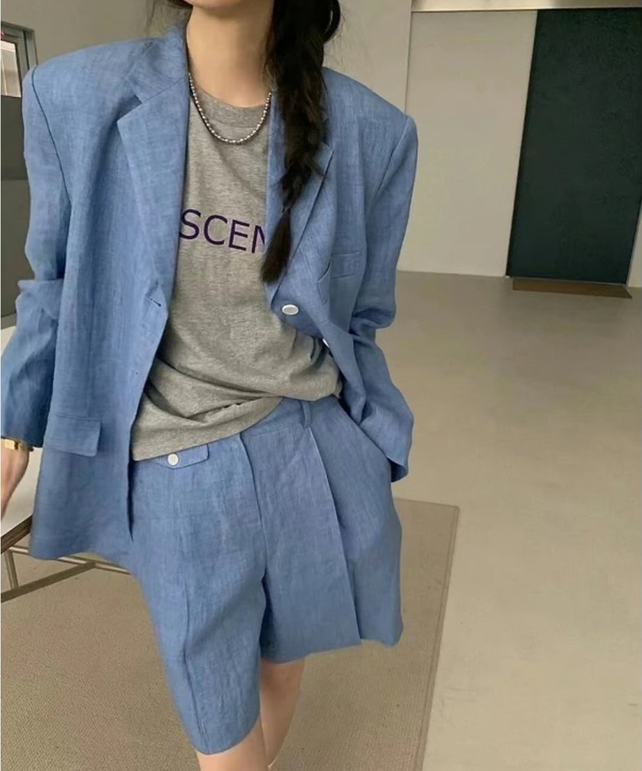 ブルーのリネン混ジャケットとバミューダパンツのセットアップを着用した女性。インナーにはグレーのロゴTシャツを合わせたショット。