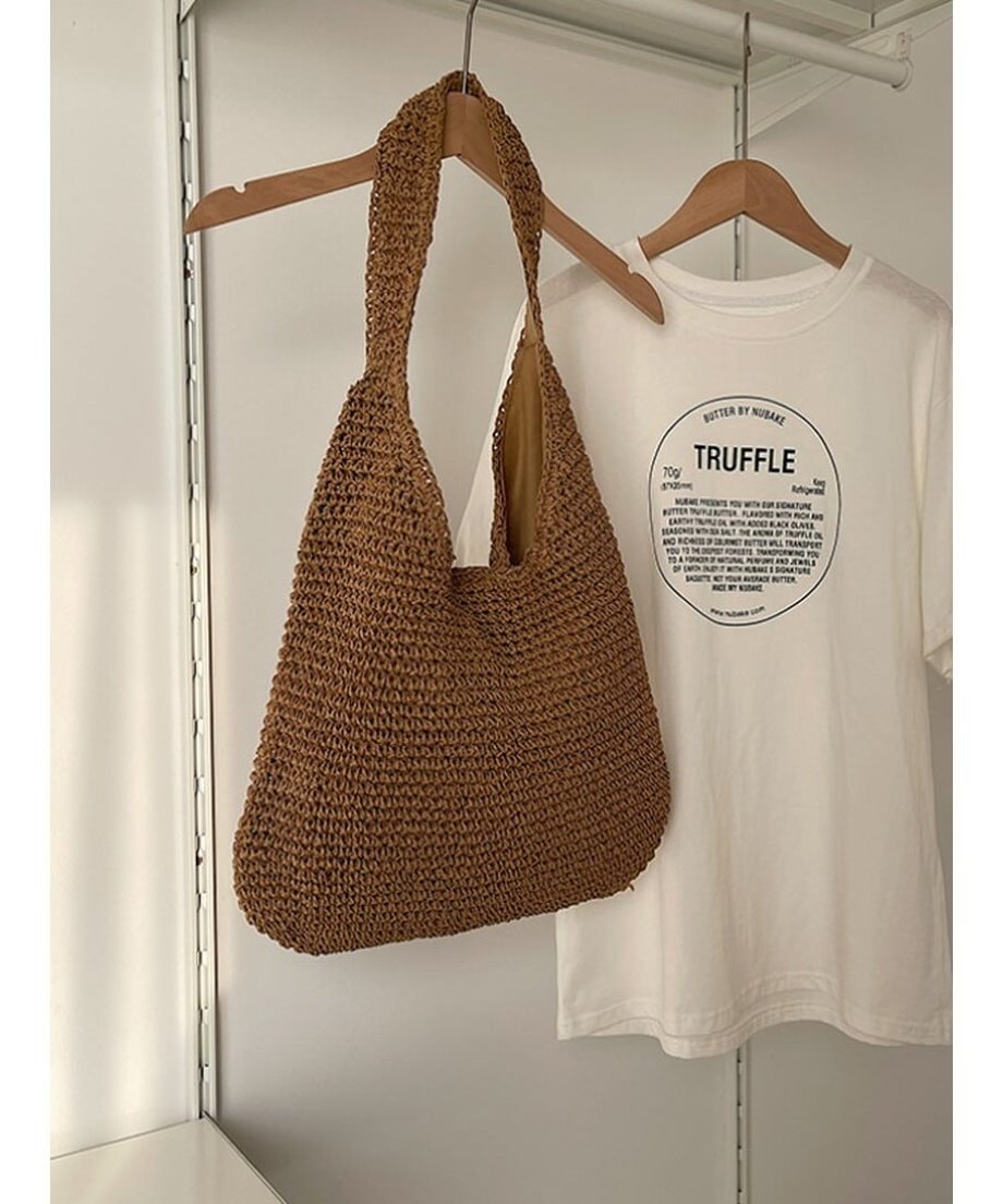 ハンガーにかけられた、白いTシャツと並ぶカーキのストローショルダーバッグ。