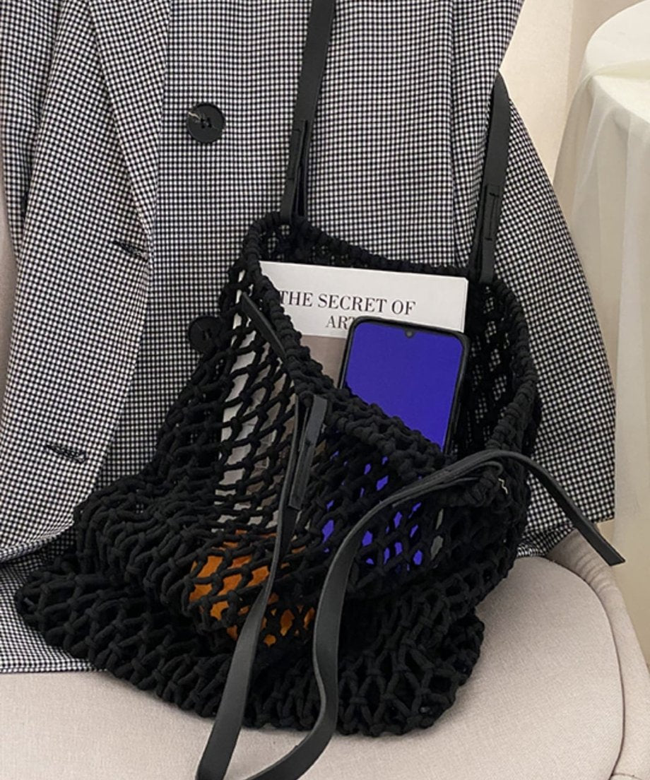 チェック柄のジャケットの横に置かれた、スマートフォンや本が入ったブラックのネット編みバッグ
