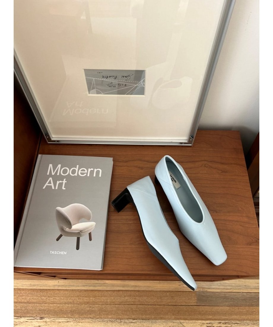 「Modern Art」と書かれた本と並んで置かれた、ブルーのスクエアトゥパンプスの俯瞰写真。