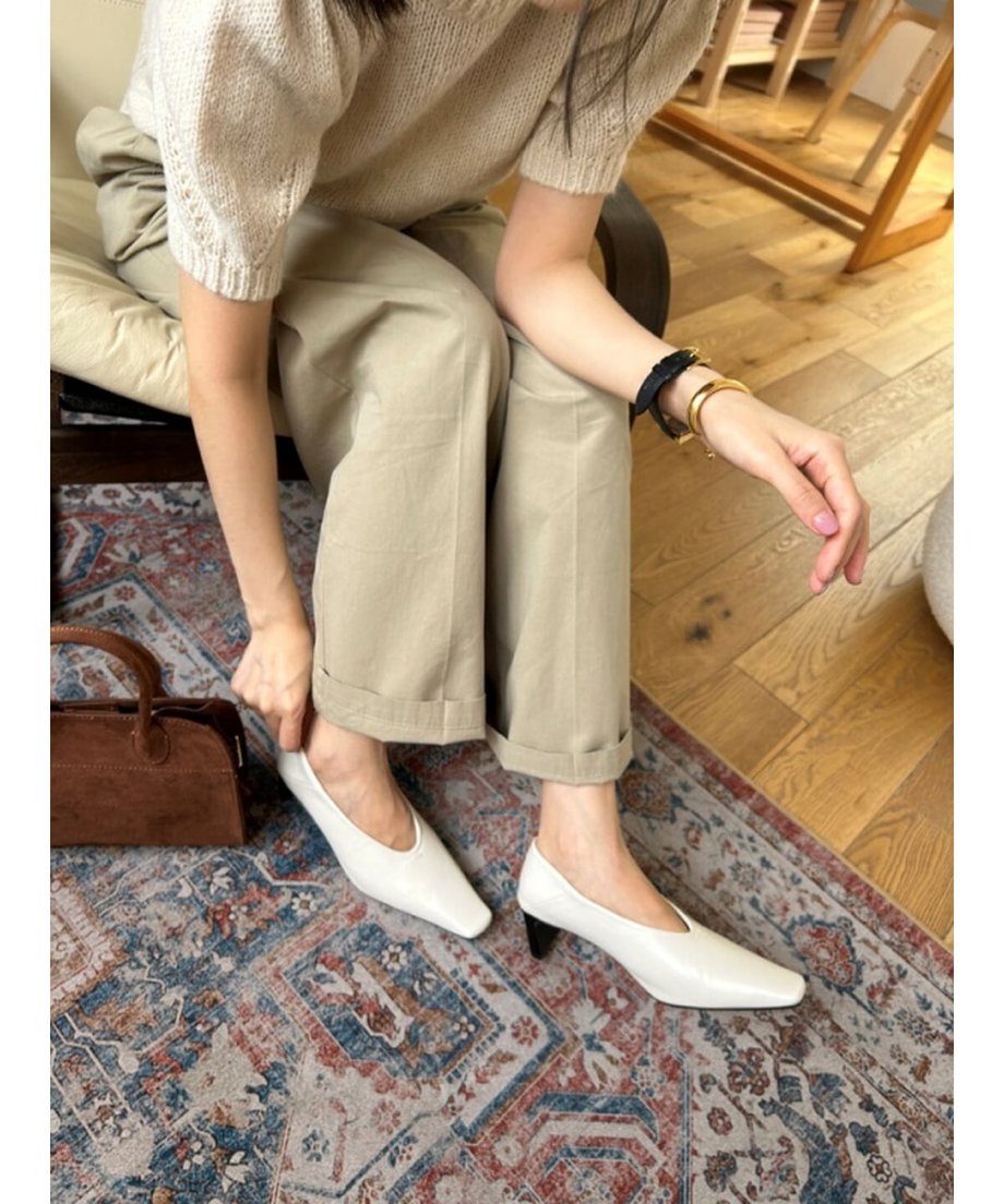 ベージュのニットとパンツを合わせた女性が、オフホワイトのパンプスを履き直しているナチュラルな雰囲気のカット。