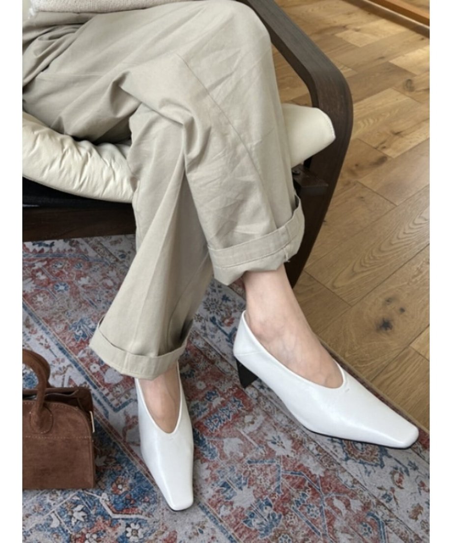 ベージュのパンツを履いた女性が、オフホワイトのVカットヒールパンプスを着用している足元のアップ。
