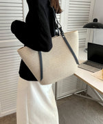 デスクの横でオフホワイトのトートバッグを肩にかけ、黒いニットを着用している女性の横姿
