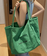 グリーンの大きなキャンバストートバッグを肩にかけた女性のショット。