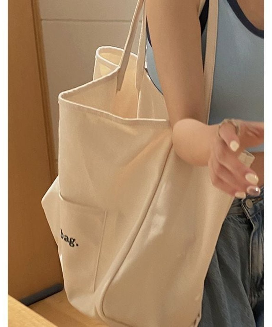 オフホワイトのビッグトートバッグを肩にかけた女性のアップショット。