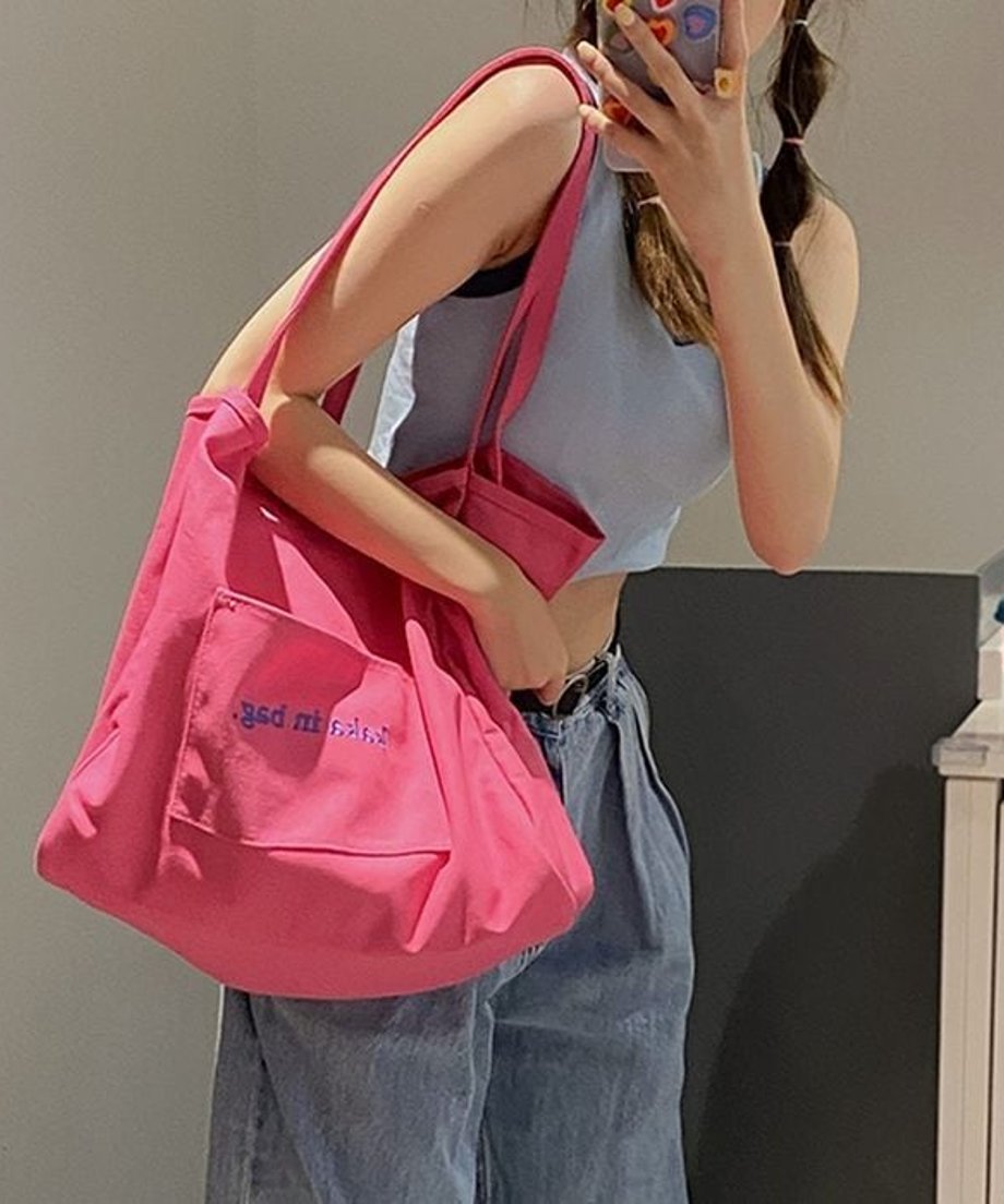 ピンク色のトートバッグを肩にかけ、スマートフォンを操作する女性の様子