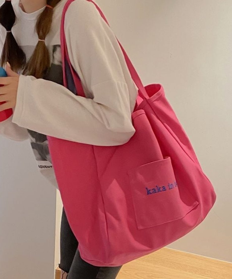 鮮やかなピンク色のロゴ入りビッグトートバッグを肩に掛けた女性のショット。