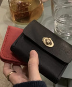 赤いケースの上に重ねて黒のレザーカードケースを持った画像。