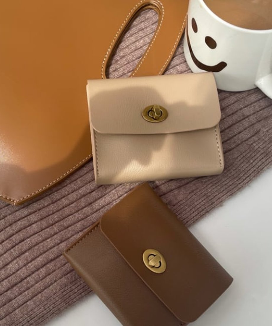 ベージュとブラウンのカードケース。背景にはコーヒーカップとバッグ。