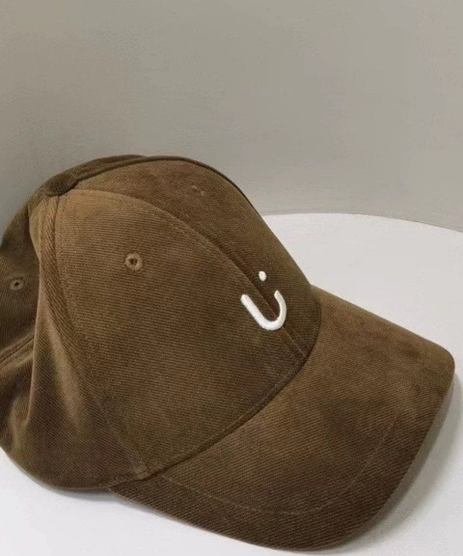 ダークブラウンのコーデュロイキャップのフロントに、Uの文字を模した白いワンポイント刺繍が施されています。