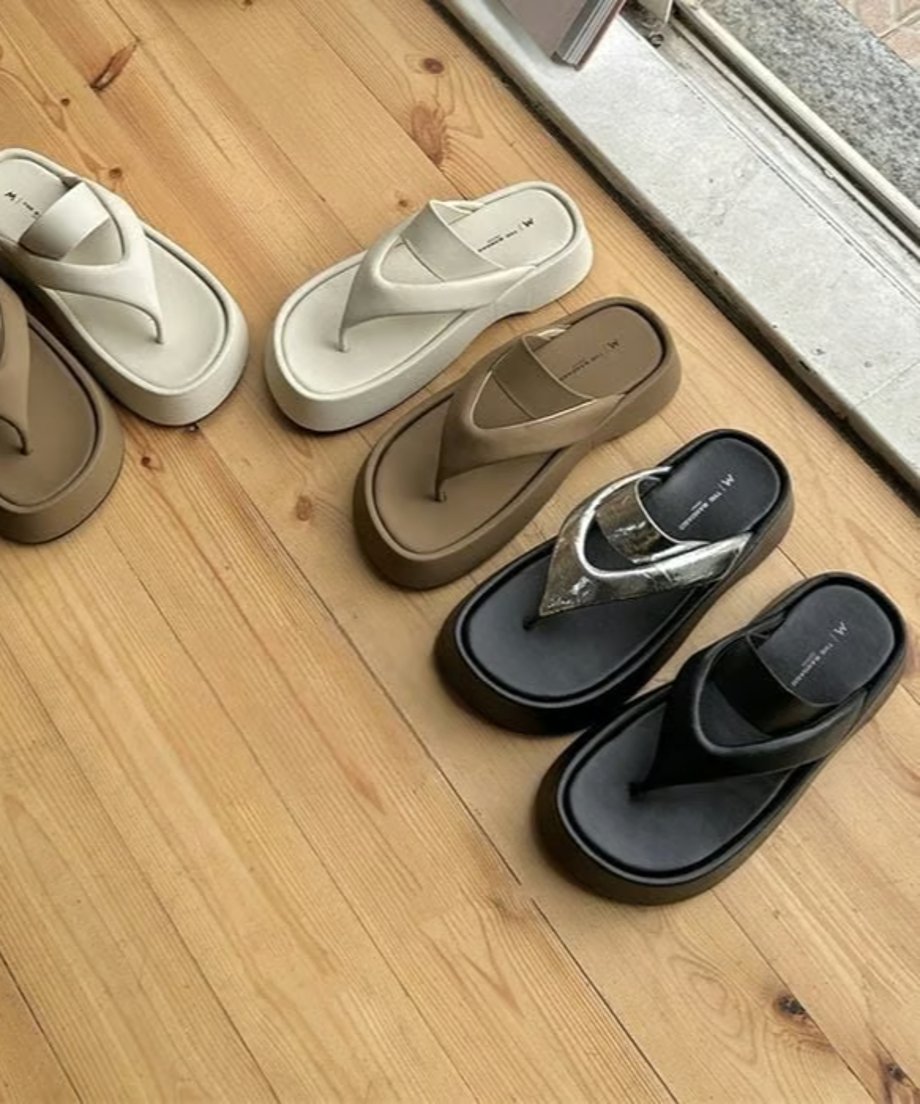 木目調の床に並んだホワイト、ブラウン、シルバー、ブラックのプラットフォームトングサンダルがランダムに置かれている。
