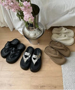 木目調の床に並んだオフホワイト、ブラウン、シルバー、ブラックのプラットフォームトングサンダル。中心に花が置かれている。