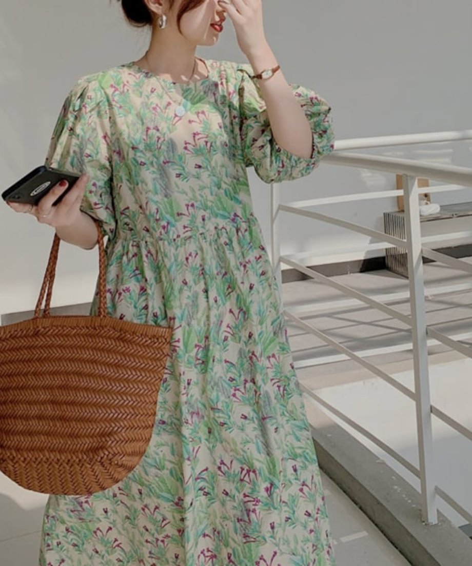 パフスリーブのボタニカル柄ワンピースに、茶色の編み込みトートバッグを手に持つ女性の立ち姿