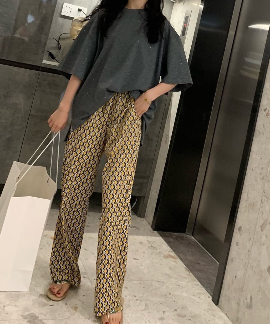 チャコールのTシャツをフロントインした女性がエレベーター前に立つリラックス感のある全身ショット。