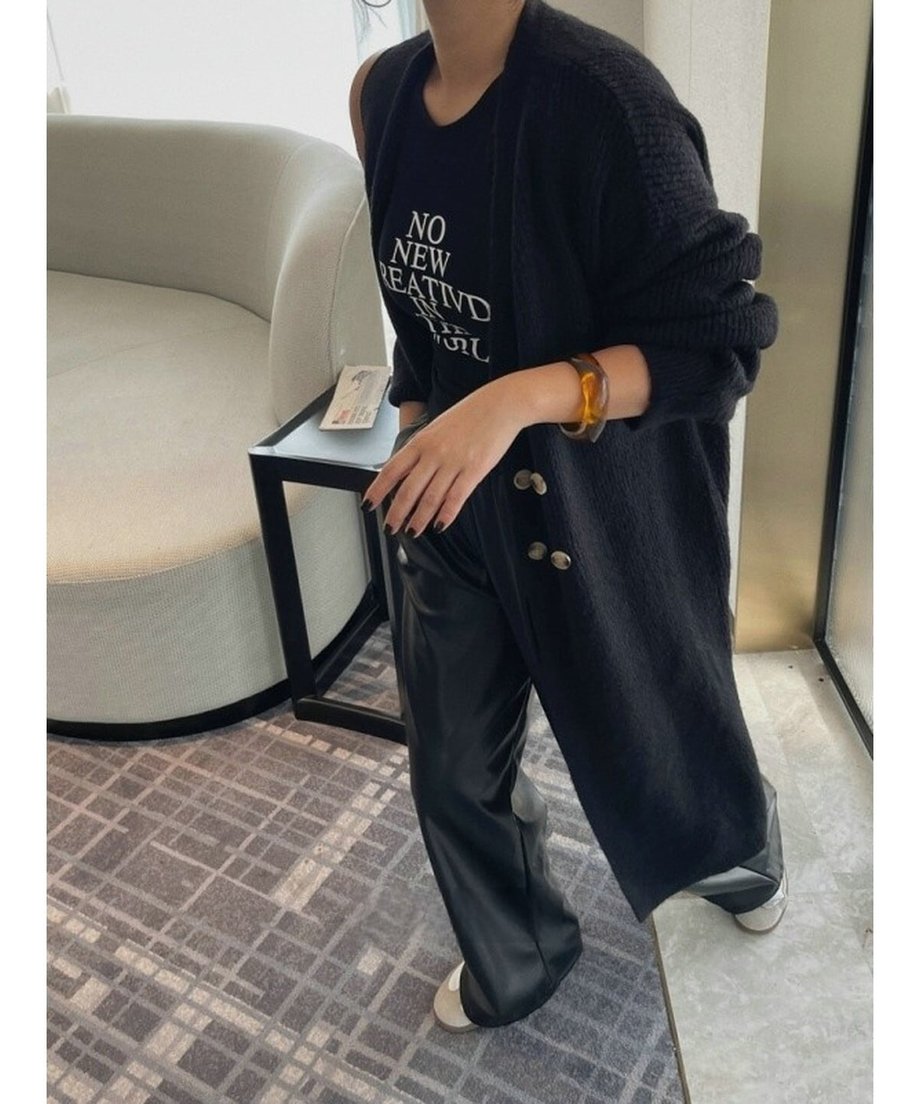 ブラックのフェイクレザーパンツに黒のロングカーディガンとロゴTシャツを合わせた女性の室内ショット。