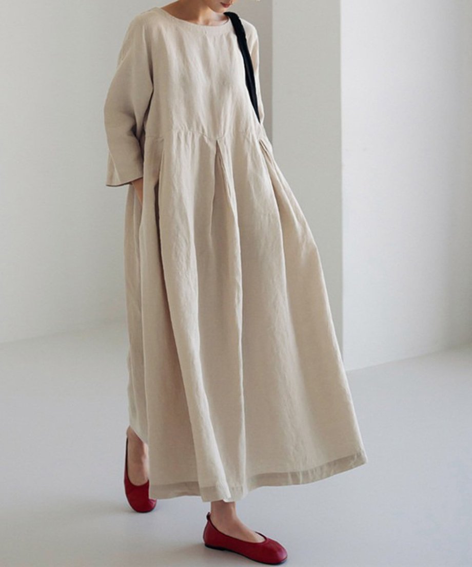 ベージュのワンピースを着用し、赤いフラットシューズを合わせたスタイリング