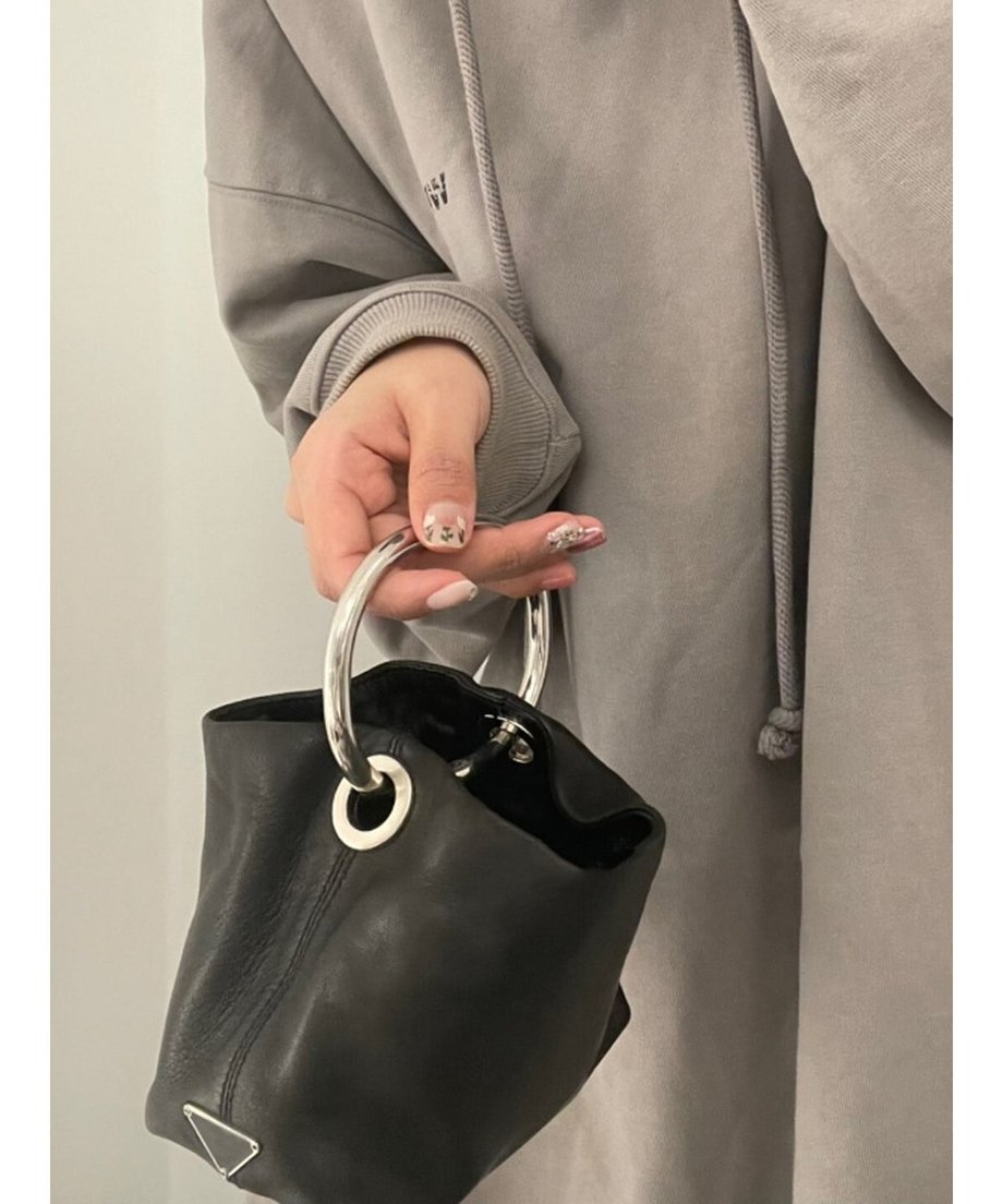 シルバーのリングハンドルを指にかけ、黒いレザーバッグを軽く持ち上げている正面からのカット。